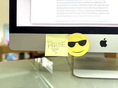 A close-up of an iMac screen with a yellow sticky note that says “PAUSE”.